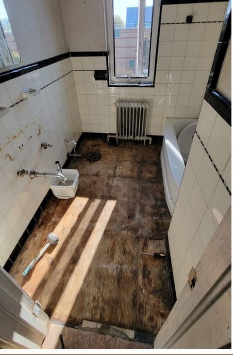 Bathroom stripped back to the subfloor with the sink disconnected and the old tile removed
