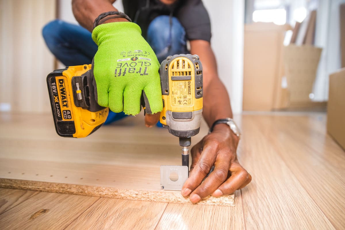 Worker fixing baseboard trim to a wall with a cordless drill