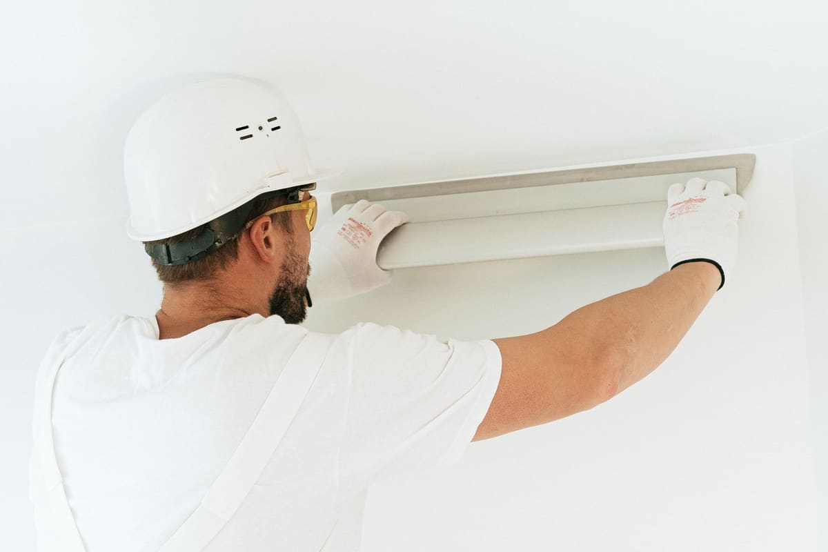 Tradesperson in a hard hat fitting a ceiling fixture in a commercial interior