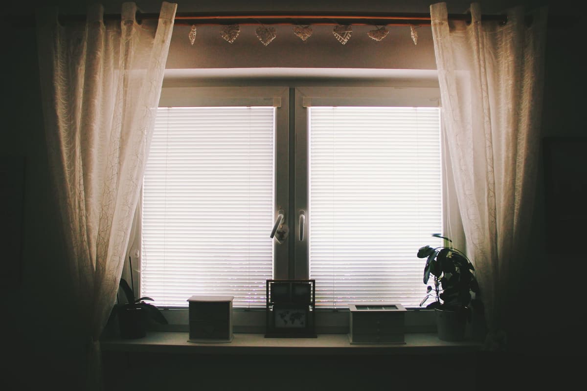 Window fitted with both a curtain rod and blinds behind the drapes