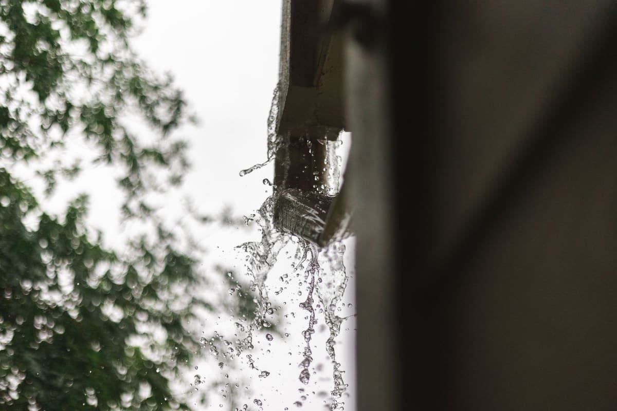 Rainwater pouring over the lip of a blocked gutter