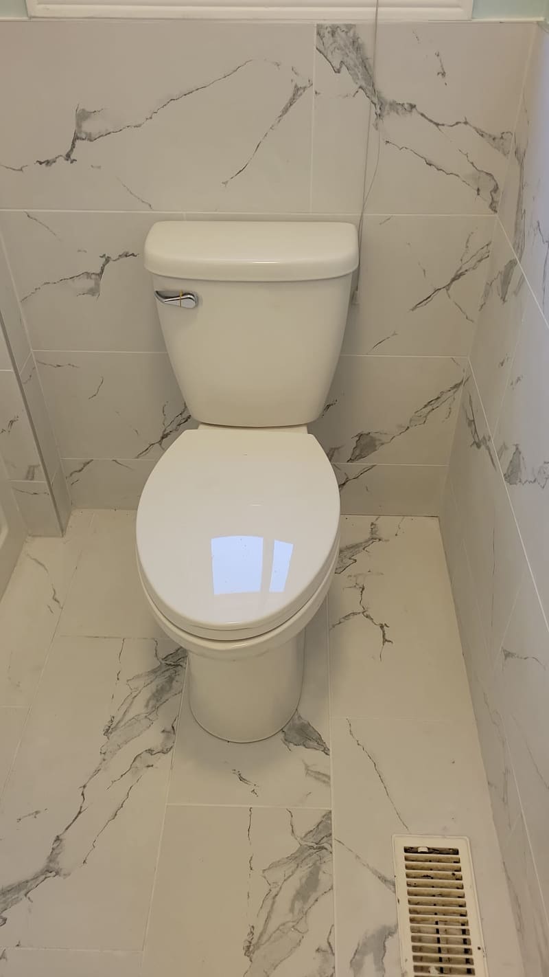 Large-format marble-look tile run floor to wall with the toilet reset on a fresh seal.