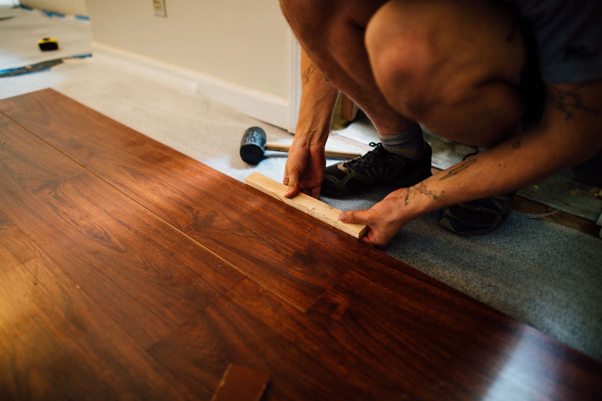 Installer fitting a dark hardwood floor board tight against the previous row