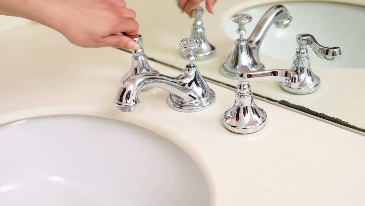 Hands tightening a chrome mixer tap onto a bathroom sink