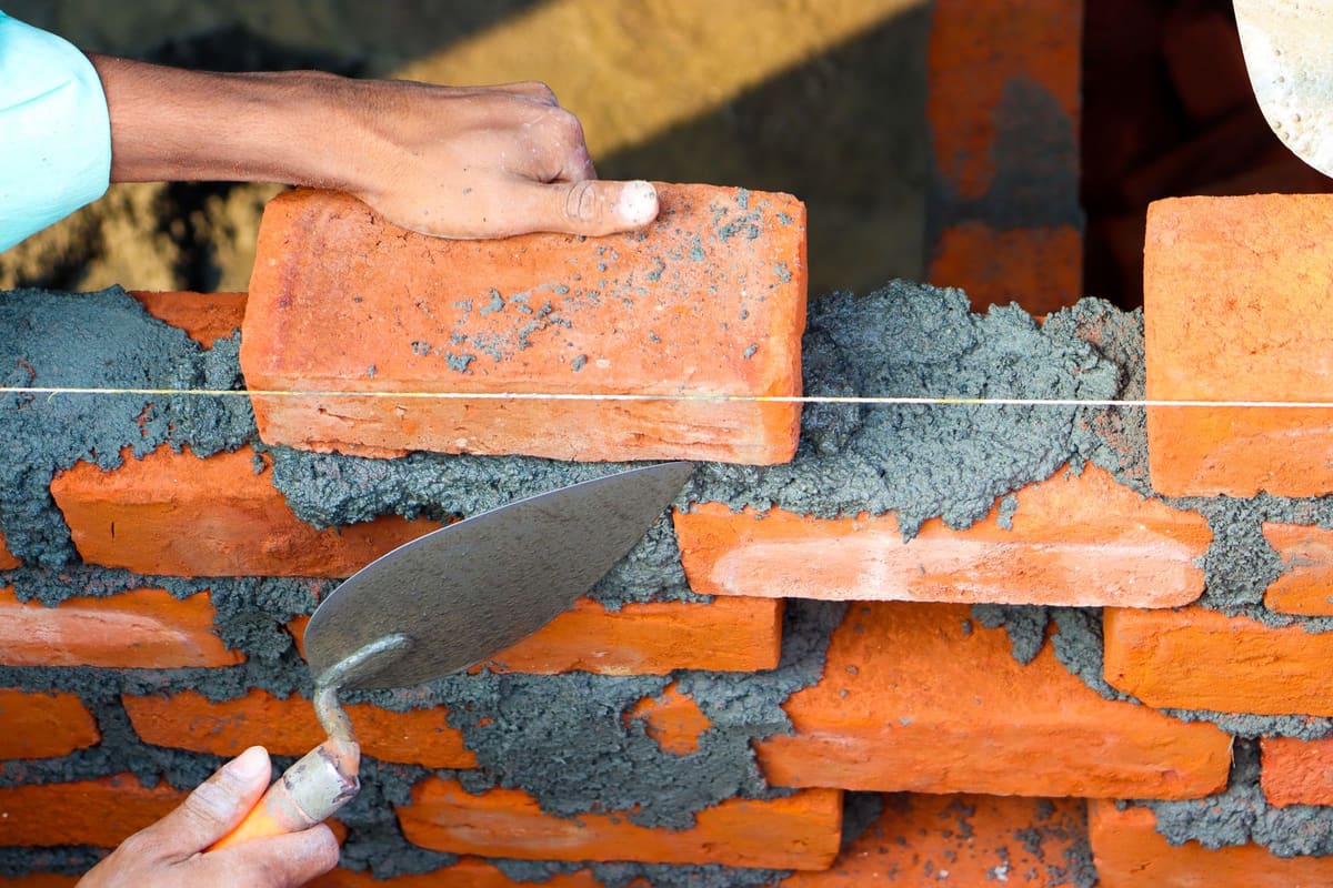 Hands bedding a brick into fresh mortar on a wall