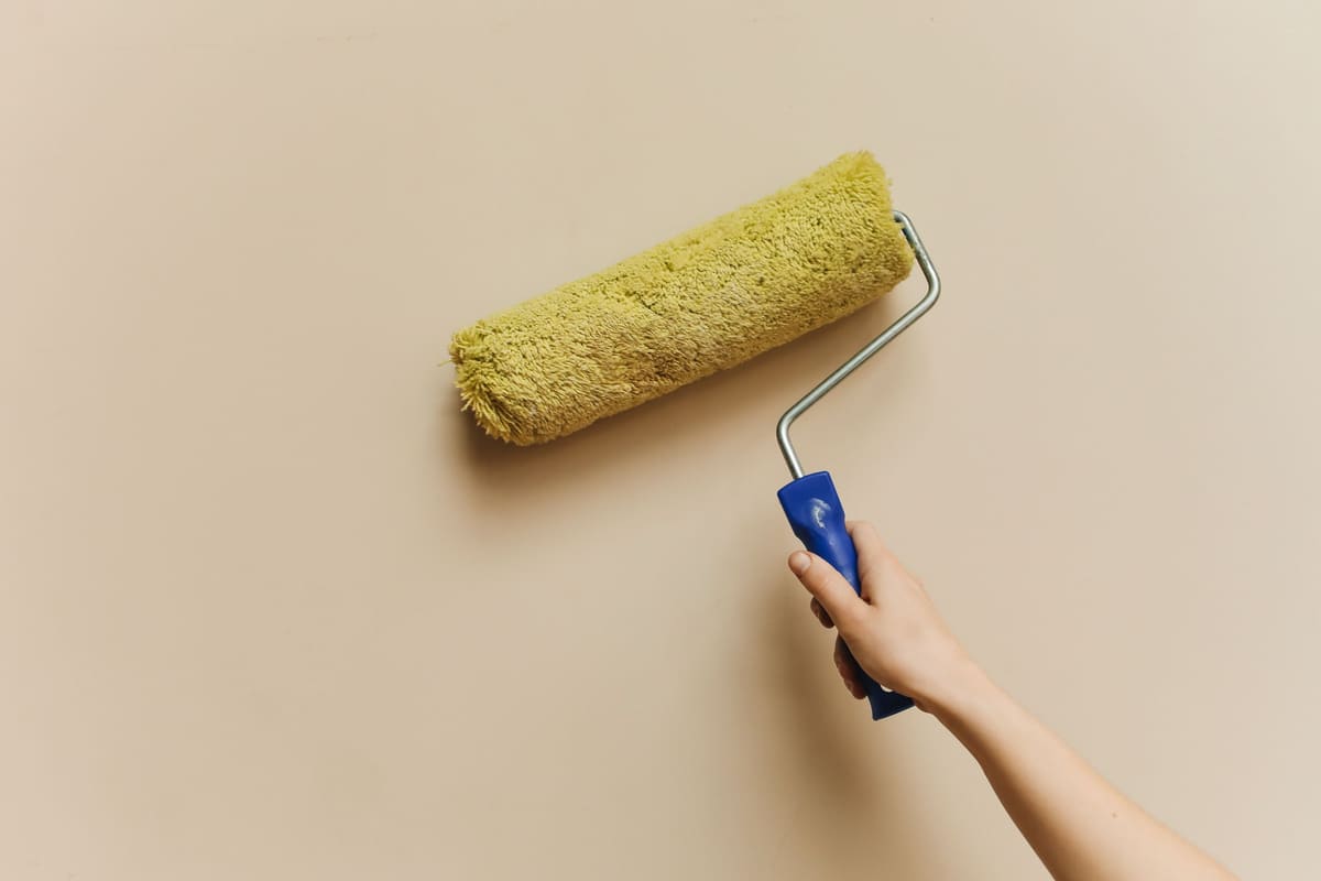 Roller loaded with paint being drawn down a flat wall