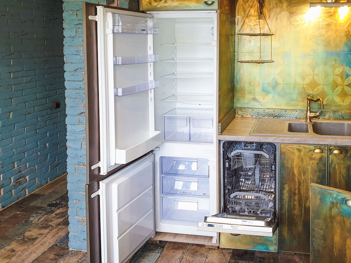 Fridge standing open in a kitchen beside a built-in dishwasher
