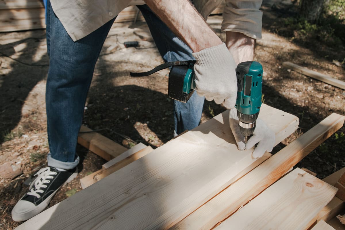 Two people fastening deck boards to a frame with a cordless drill outdoors