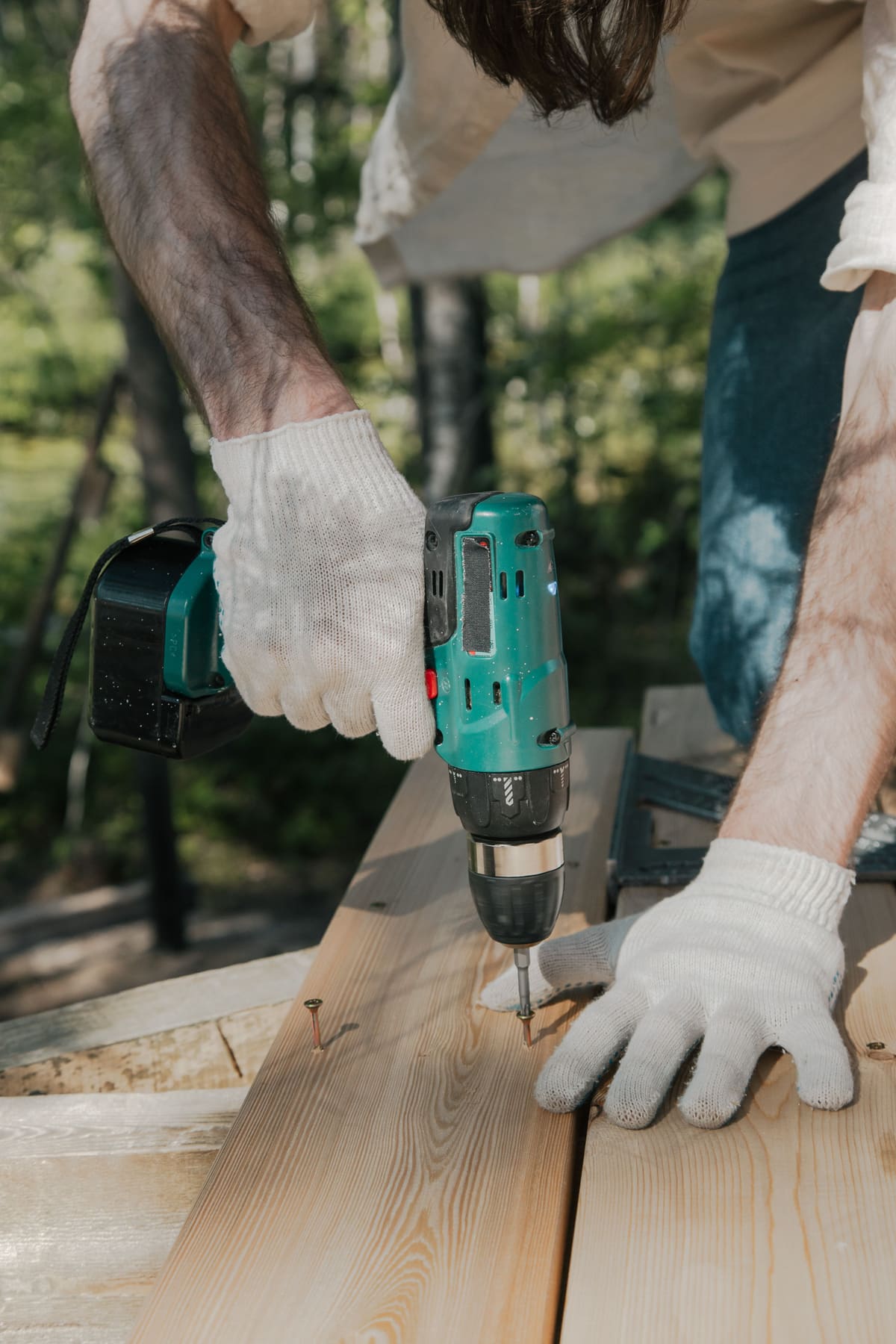 Gloved hands driving a screw into a timber rail outdoors