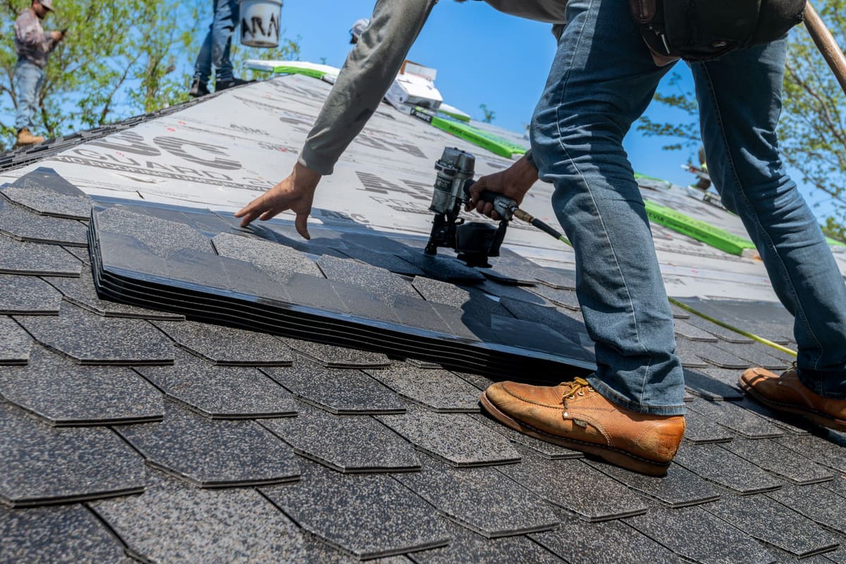 Roofer fastening asphalt shingles to a roof deck with a nail gun
