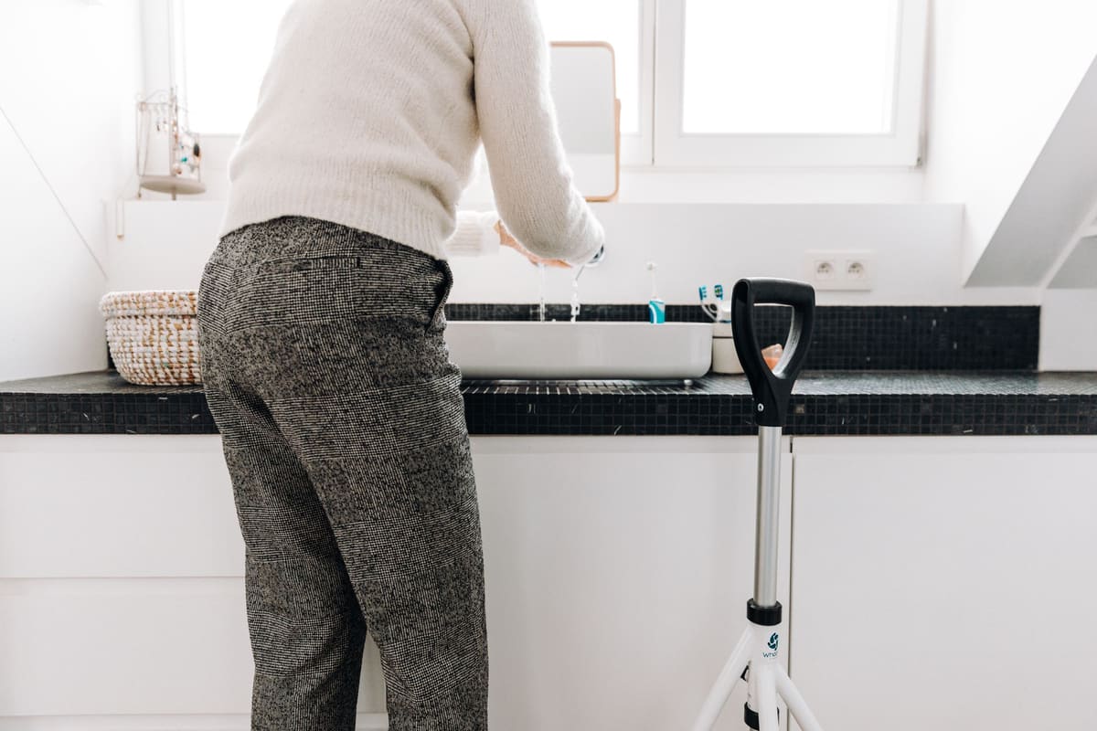 Older adult standing at a bathroom counter with a walking aid beside them