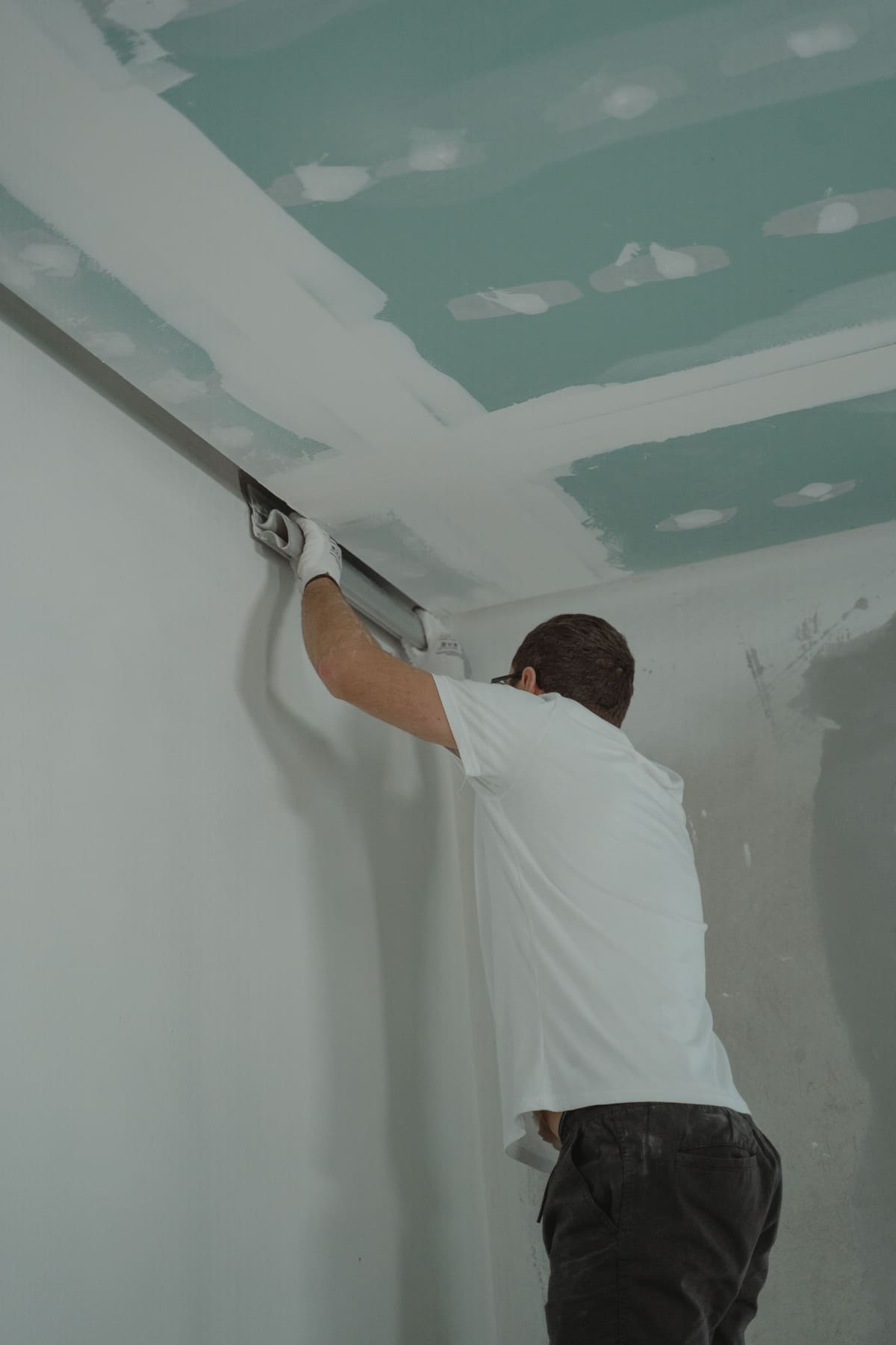 Tradesperson running a taping knife along a drywall seam near the ceiling