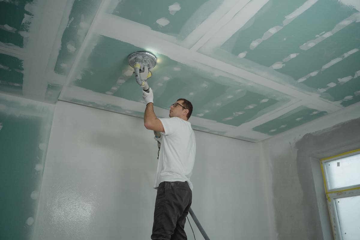 Tradesperson finishing a drywall ceiling around a light fitting