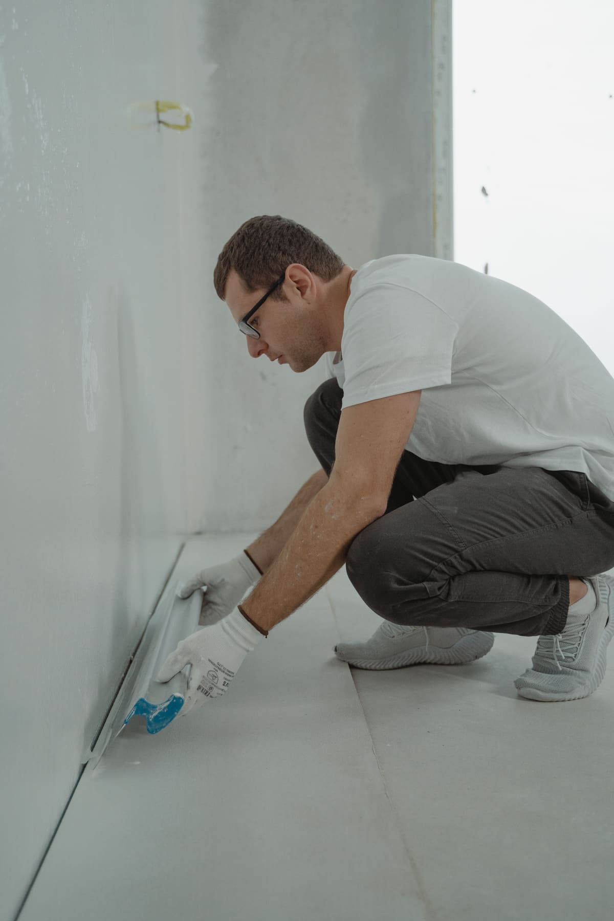 Tradesperson crouched at the base of a wall working with a tool in hand