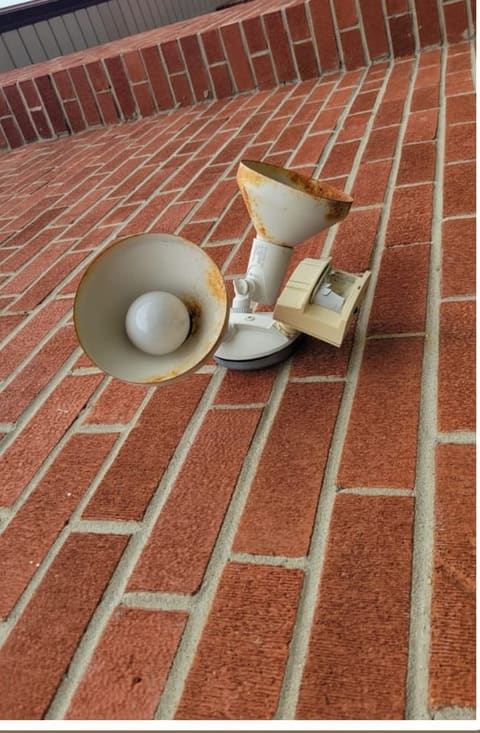 Rusted exterior light fitting and corroded vent hood on a brick wall